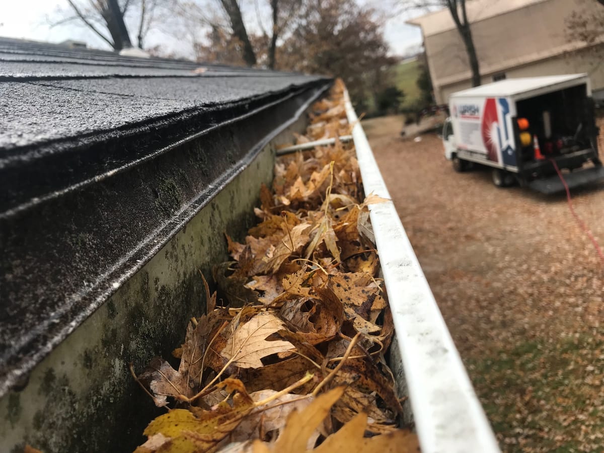 Gutter packed with fallen leaves along a shingle roof, Wash Authority truck parked in the driveway